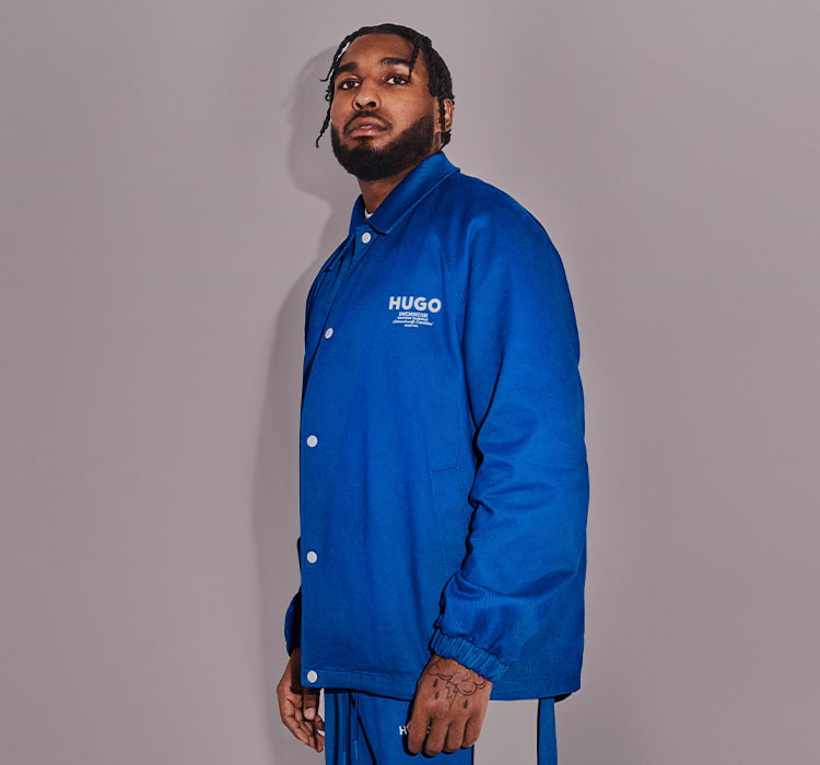 HUGO BLUE – Reezy dressed in blue, posing in front of a gray background (photo)